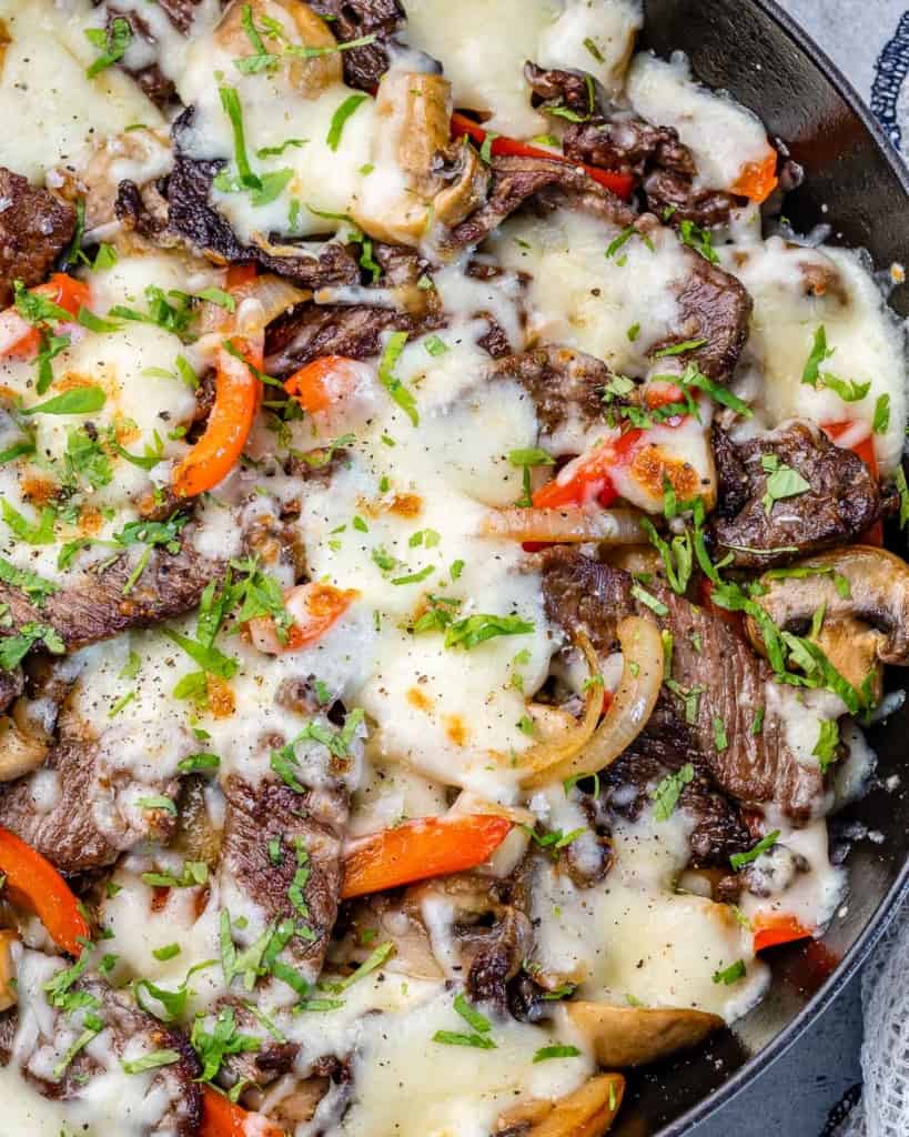 top view of philly steak in skillet with onion, bell pepper, mushrooms, cheese, and cilantro