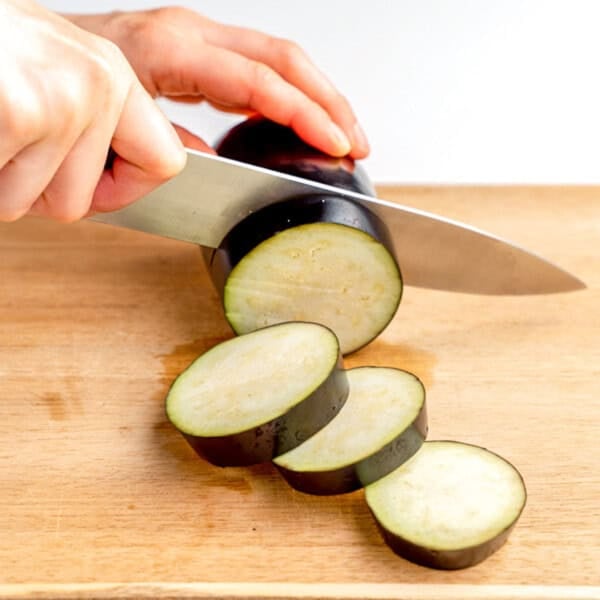 slicing an eggplant on a cutting board.