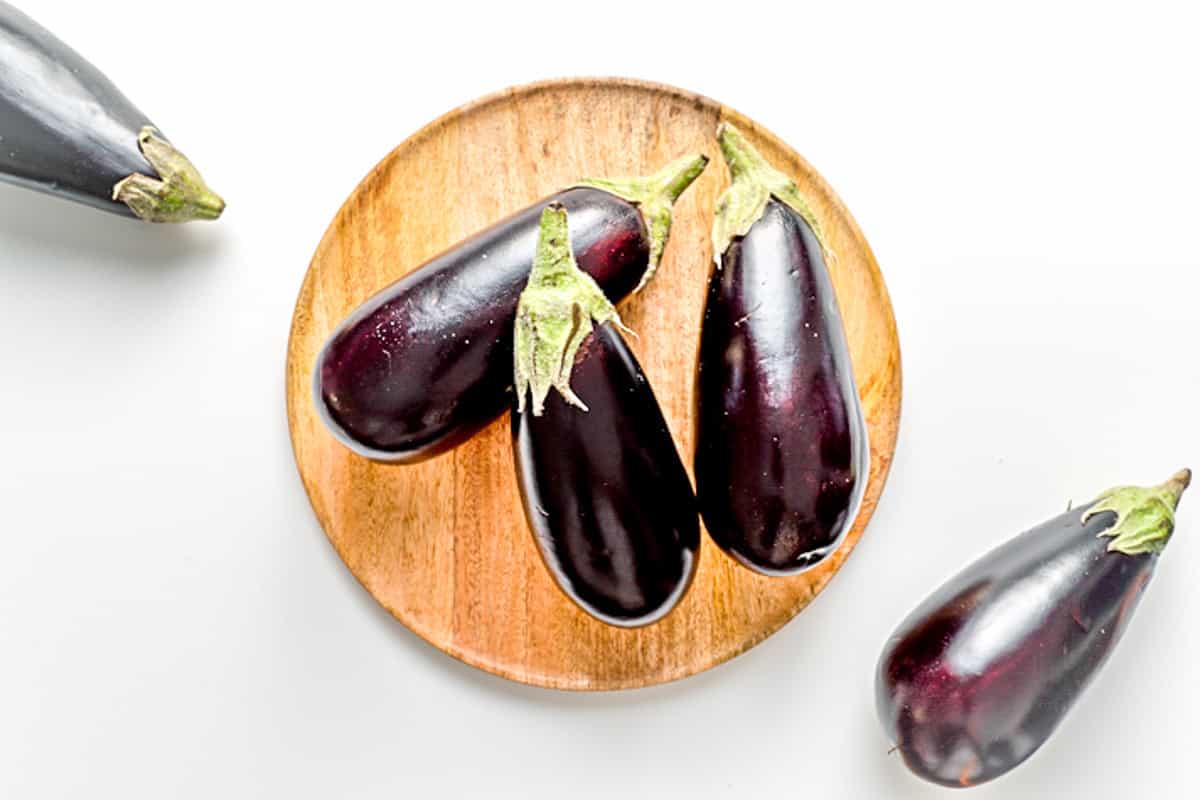 whole eggplants on a round cutting board.