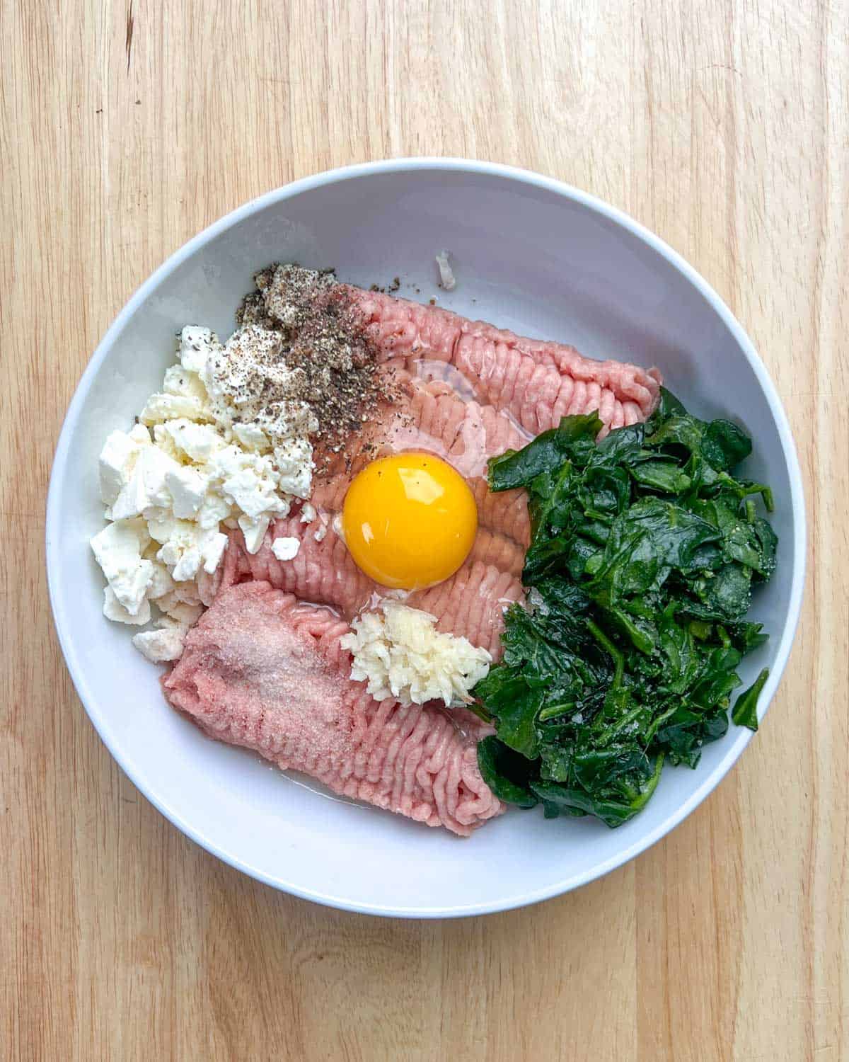 ground turkey, egg, spinach, feta cheese, and seasonings, added to a bowl.