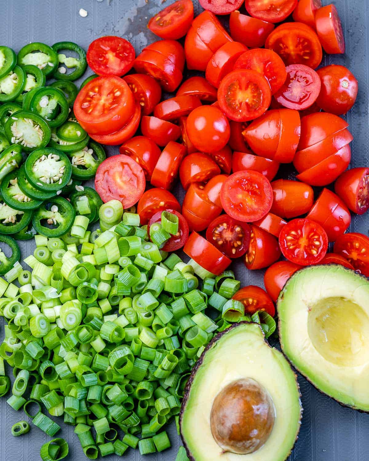 chopped green onions, tomatoes, jalapeño peppers, and avocado on cutting board