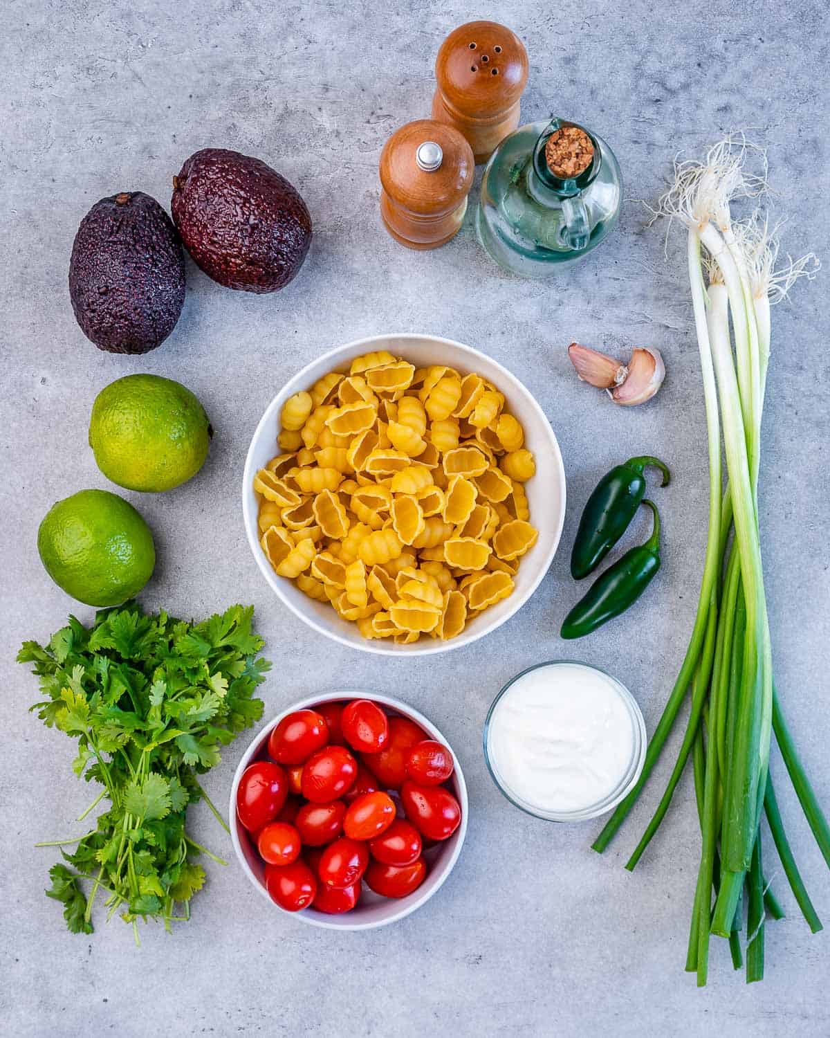 pasta, Greek yogurt, green onions, jalapeño peppers, garlic cloves, salt, pepper, avocados, limes, cilantro, and cherry tomatoes for pasta salad