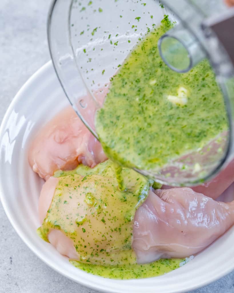 Pouring cilantro lime marinade over raw chicken breasts.