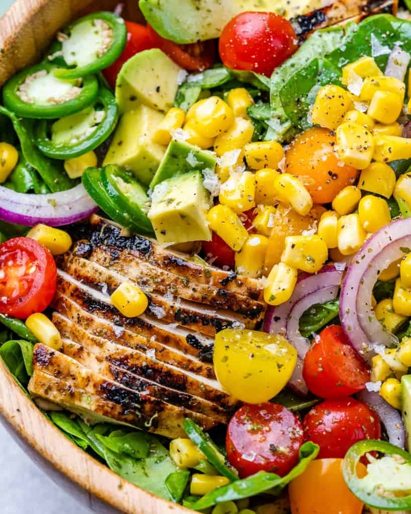 Sliced grilled chicken served over a salad with corn and sliced jalapeños.
