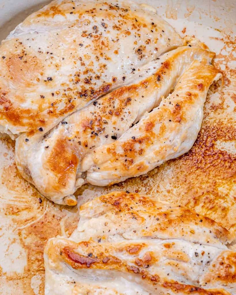 Chicken breasts cooking in a large skillet.