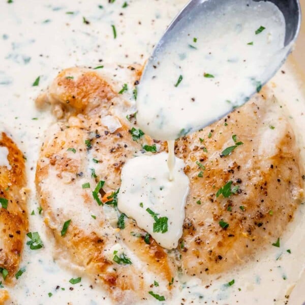 chicken breast in a garlic creamy sauce with spoon pouring sauce over chicken
