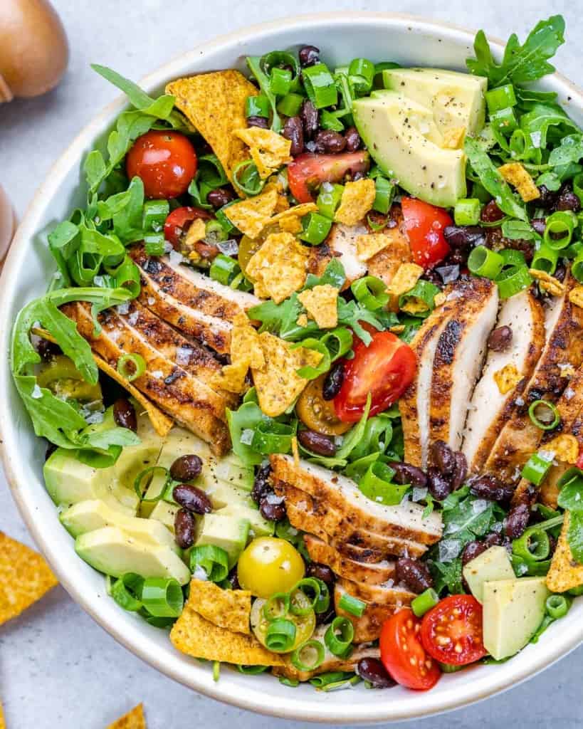 top view of salad topped with sliced grilled chicken in a white bowl
