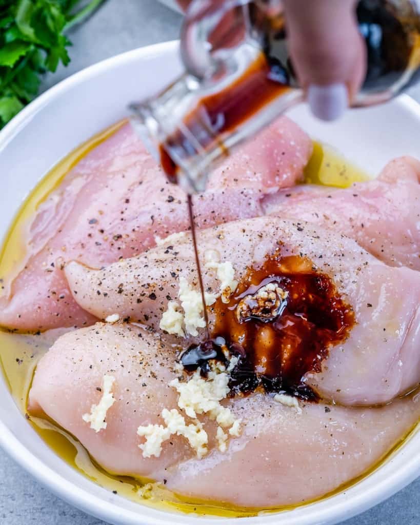 Pouring balsamic vinegar over raw chicken breasts.