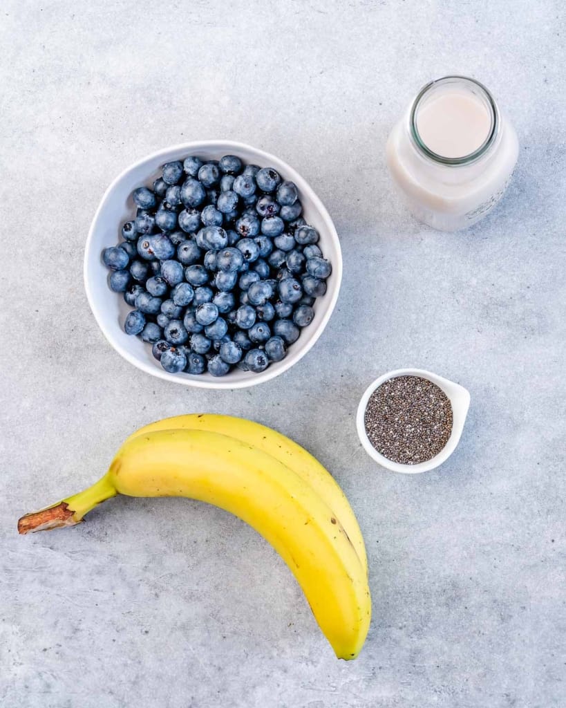 Blueberries in a bowl with a banana, small bowl of chia seeds and jar of milk.