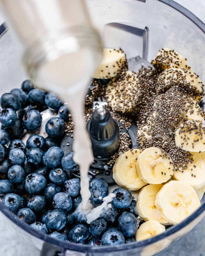 Pouring milk into a blender with blueberries, bananas and chia seeds.