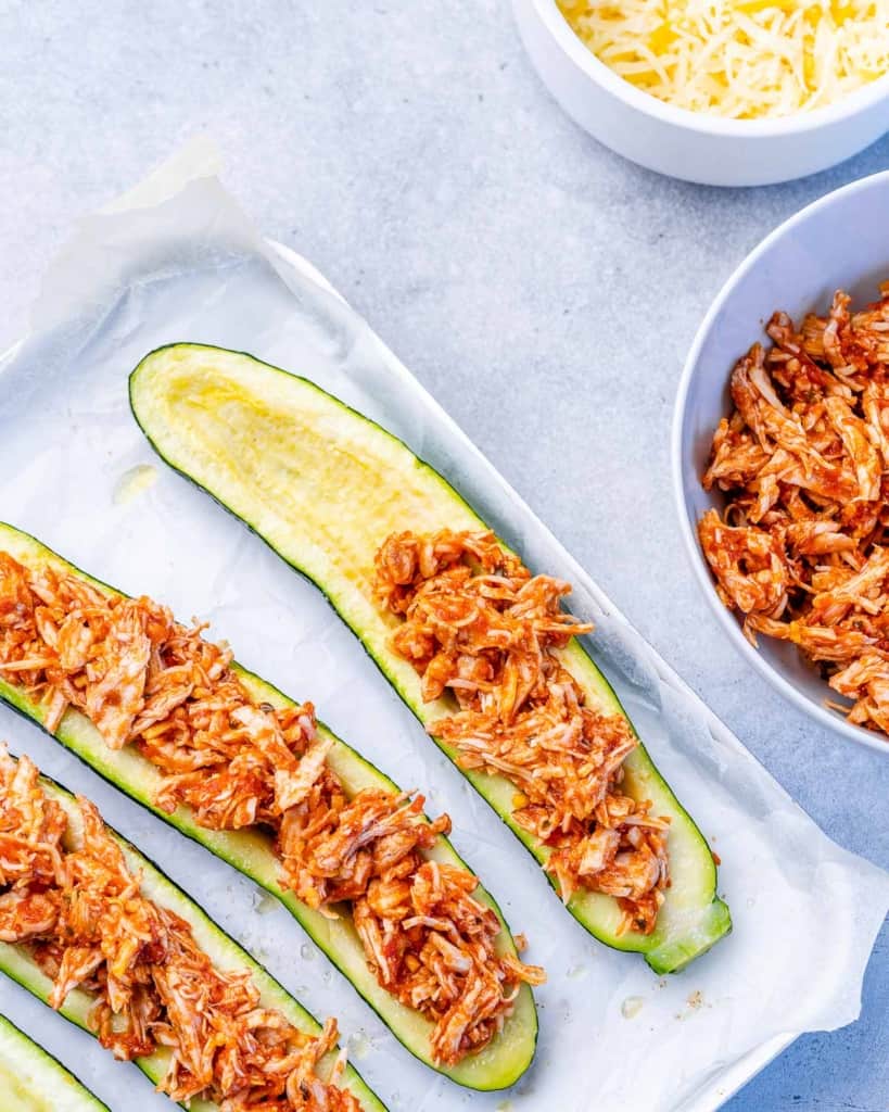 Filling zucchini halves with shredded chicken.
