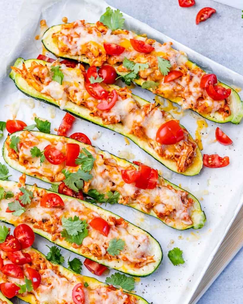 top view of zucchini boats topped with tomatoes on a white plate