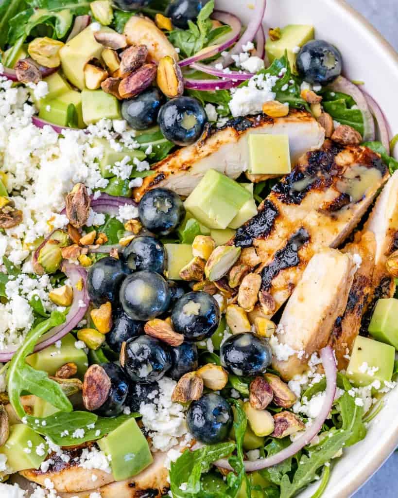 Salad topped with grilled chicken, avocado and blueberries.