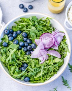 Topping arugula with blueberries and red onion.