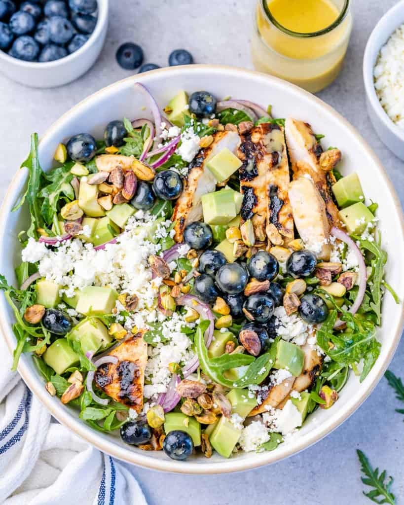 Arugula salad topped with chicken, blueberries and feta cheese.