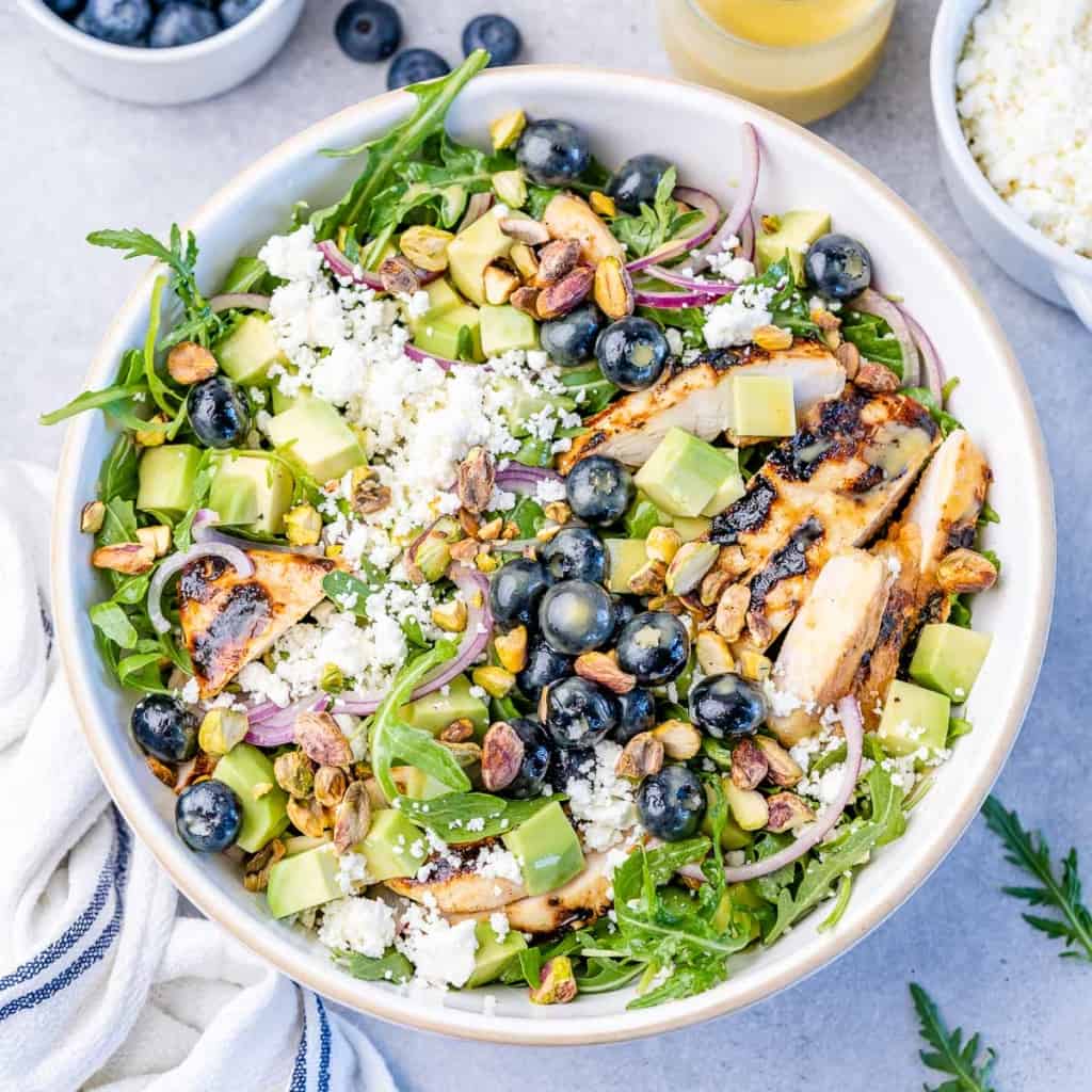 top view grilled chicken salad topped with cheese, blueberries, and nuts