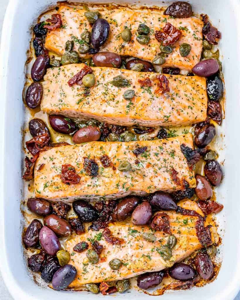top view baked salmon in a white baking dish, topped with olives