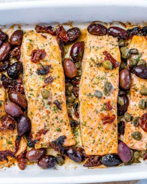top view of baked salmon filets in a white baking dish topped with olives and capers