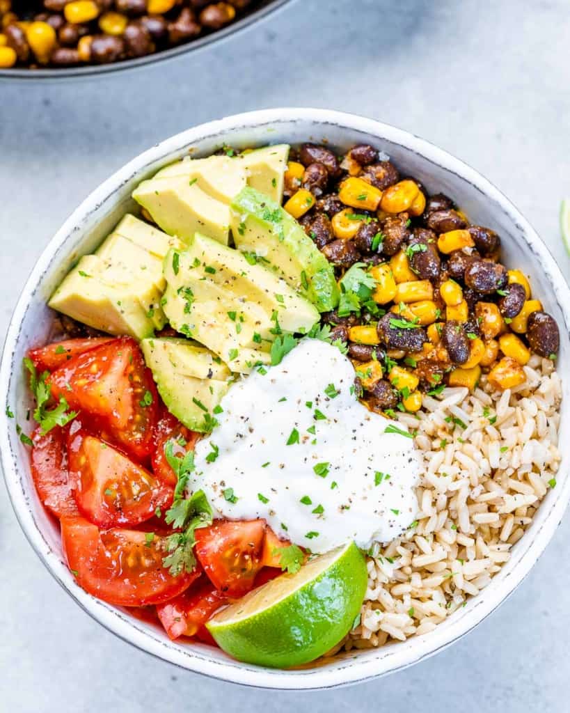 White bowl filled with rice, black beans, corn and topped with sour cream.