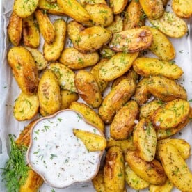 top view of baked potato wedges with a bowl of greek dipping sauce