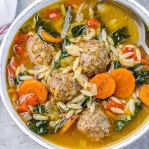 a round white bowl with meatball soup with carrots and orzo pasta.