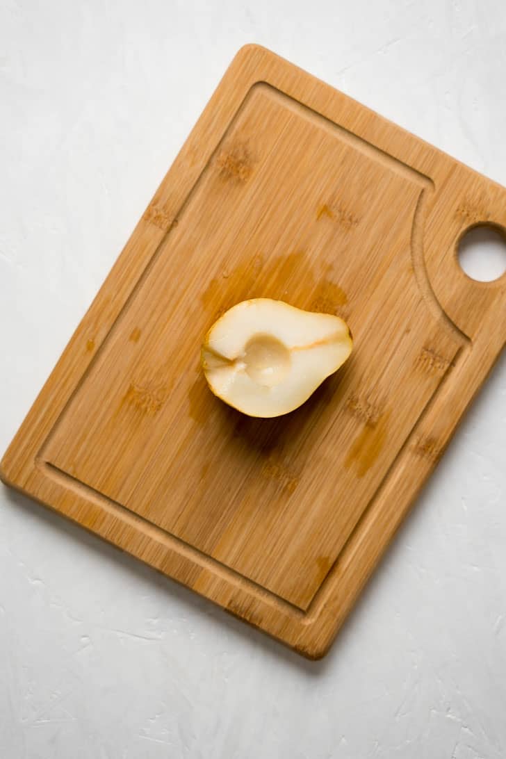 one pitted pear resting on wooden board 