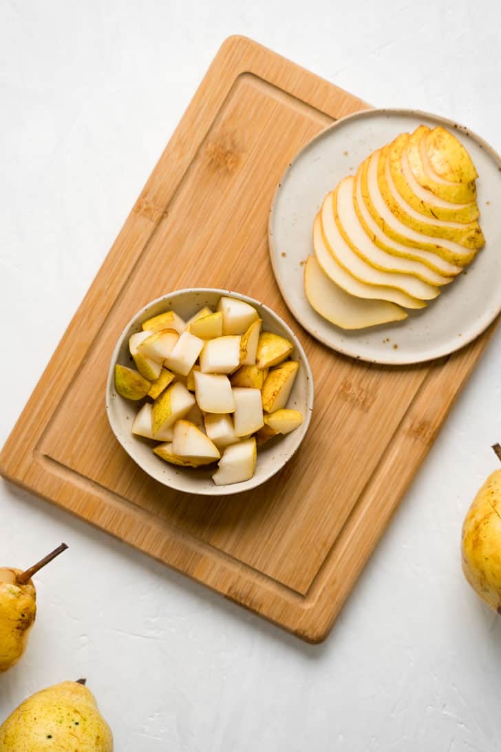 one bowl of cubed pear next to pear slices on plate with wooden board