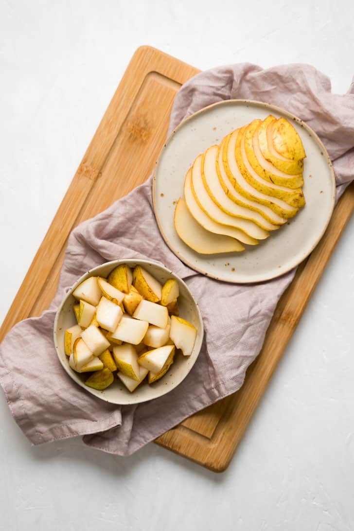 one plate with sliced pears next to bowl of pear cubes on cutting board with napkin 