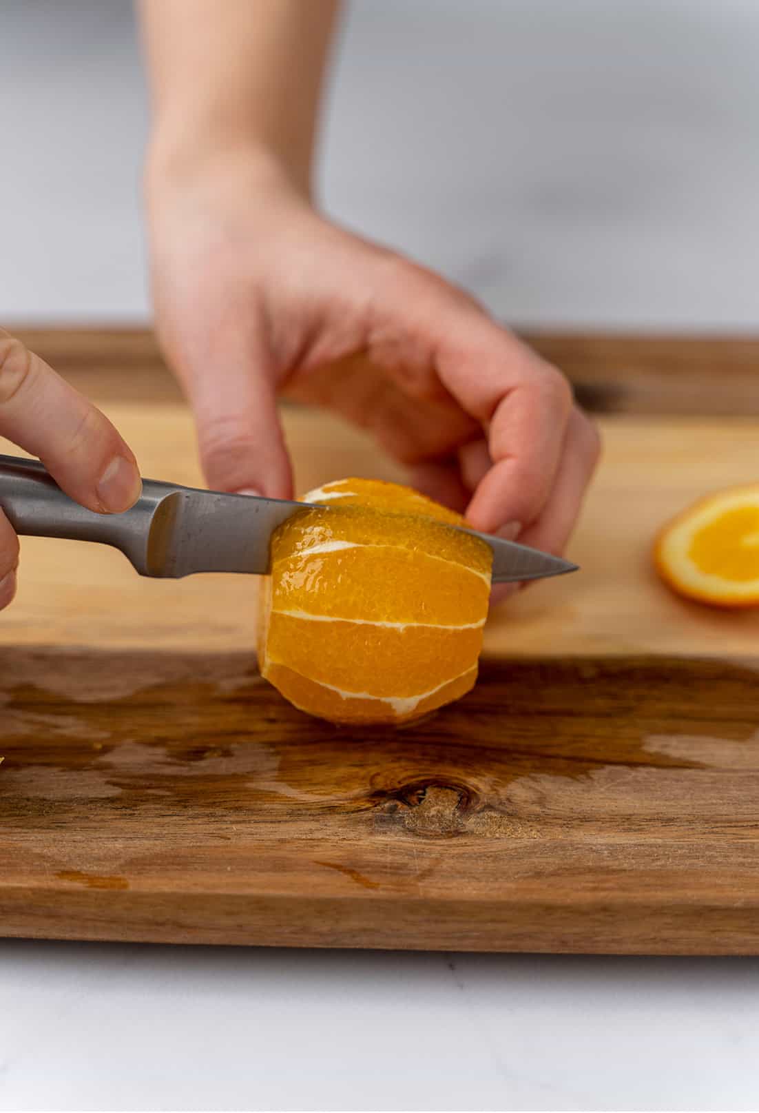 slicing through the orange with knife on cutting board 