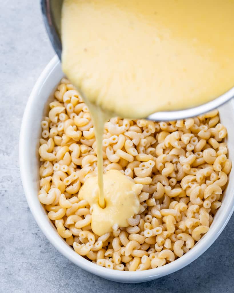 Pouring cheese sauce over elbow noodles.