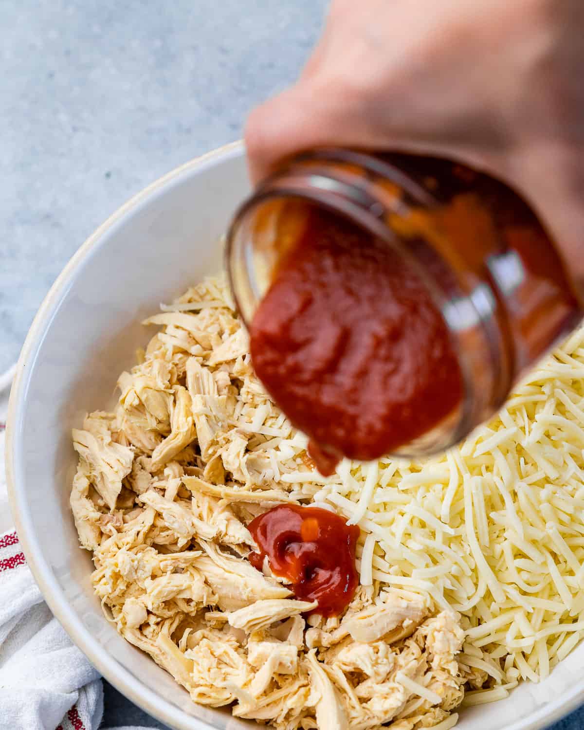 Pouring enchilada sauce into bowl of shredded chicken. 