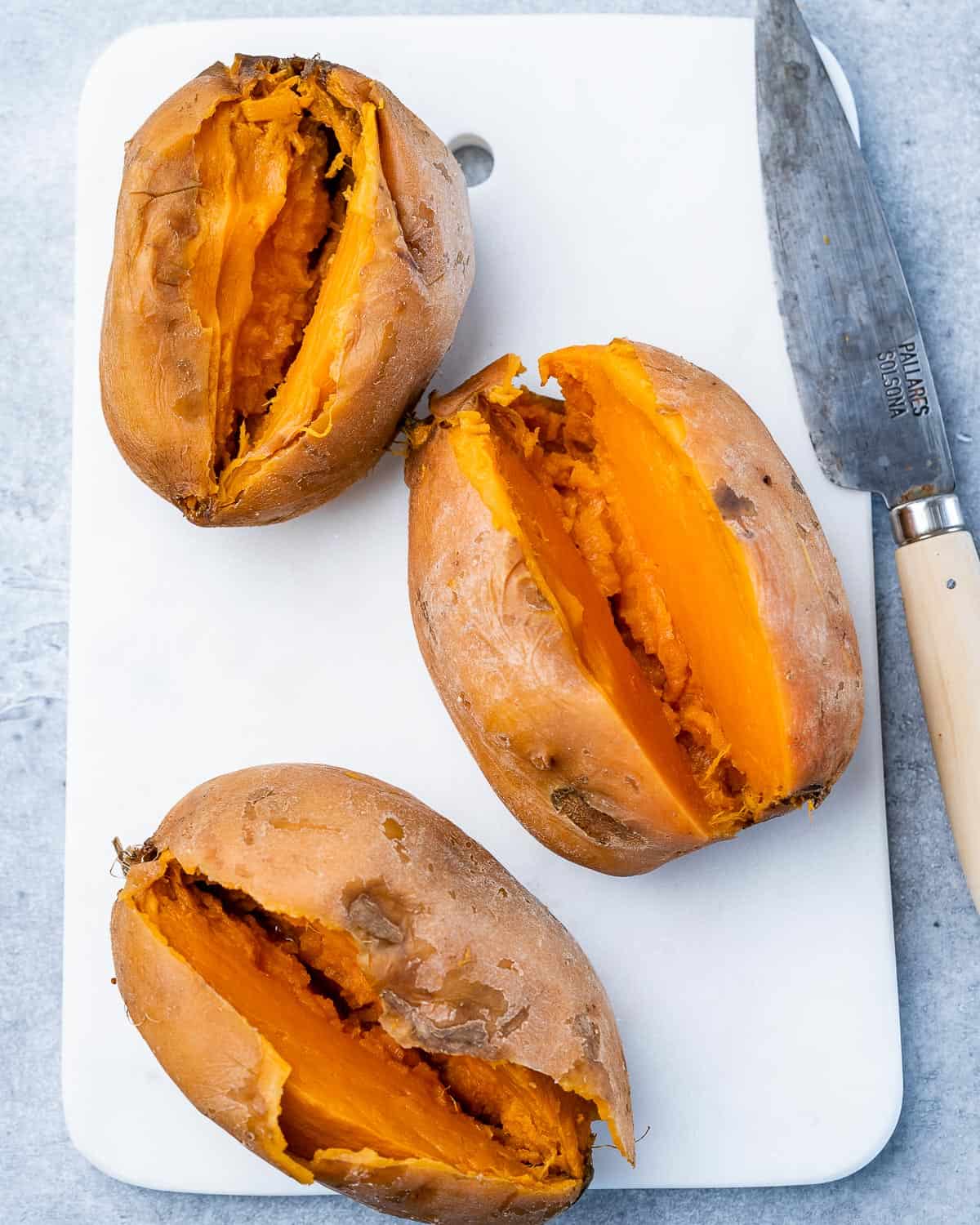Cooked sweet potatoes sliced open on a cutting board.