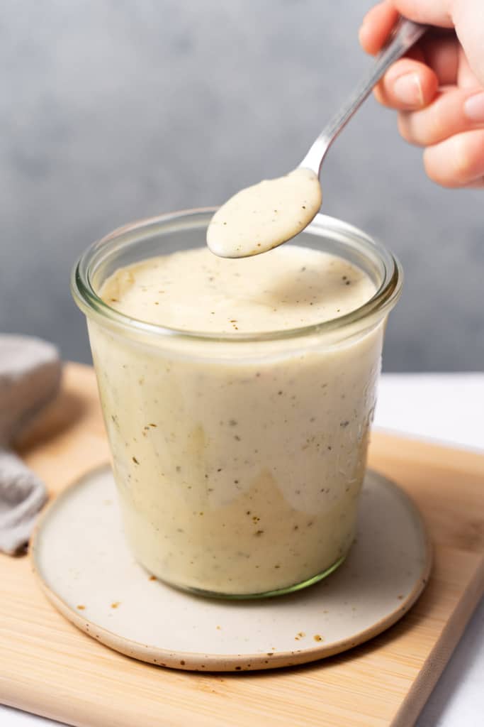Woman's hand spooning Alfredo Sauce from a glass jar.
