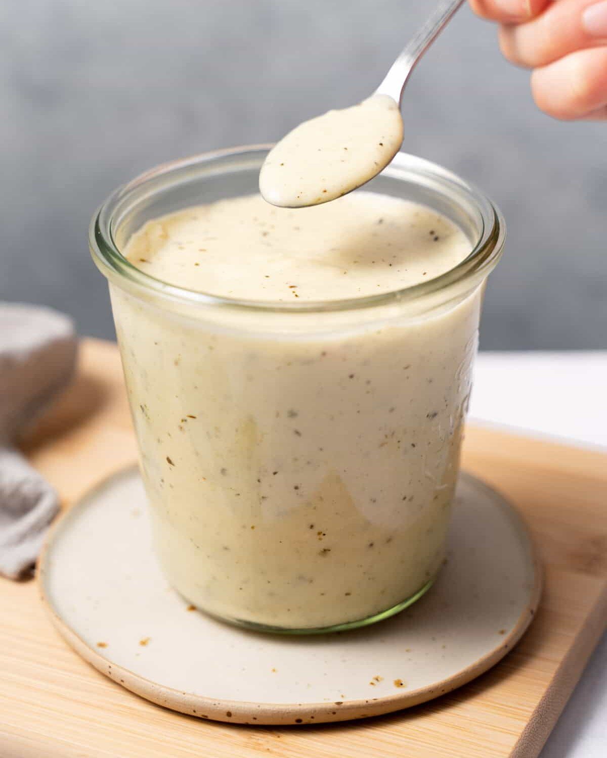 Woman's hand spooning Alfredo Sauce from a glass jar.