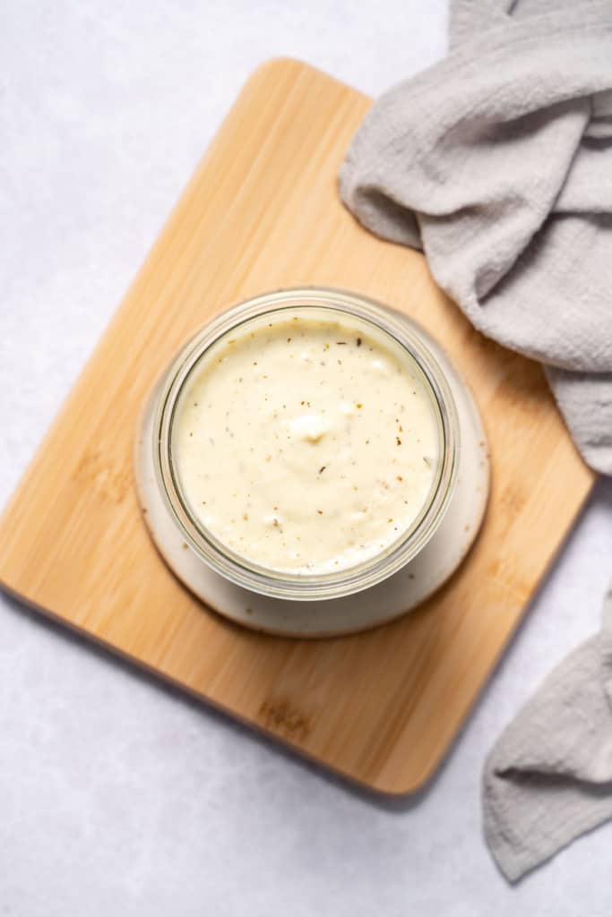 White cream sauce in a jar on a cutting board.