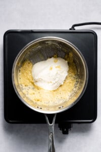 Adding cream cheese into pot with garlic and flour mixture.