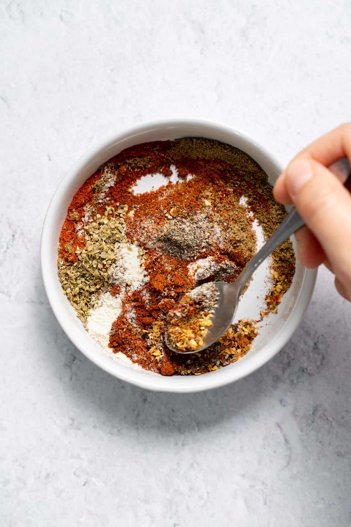 mixing ground spices in bowl with spoon for DIY taco seasoning