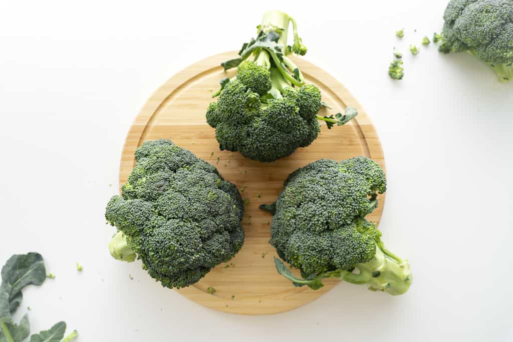 Three heads of broccoli on a cutting board.