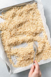 spreading breadcrumbs on baking sheet with spoon