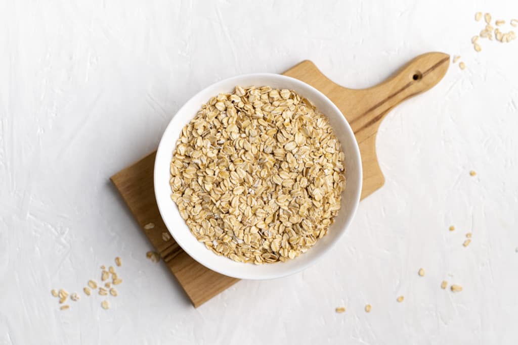 A white bowl with rolled oats on a wooden cutting board.