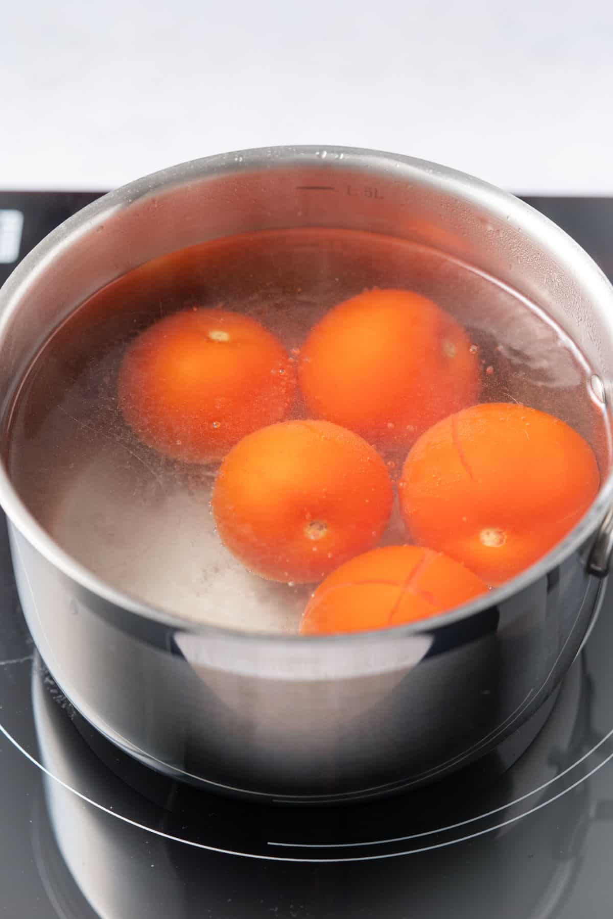 five tomatoes in a pot of boiling water 