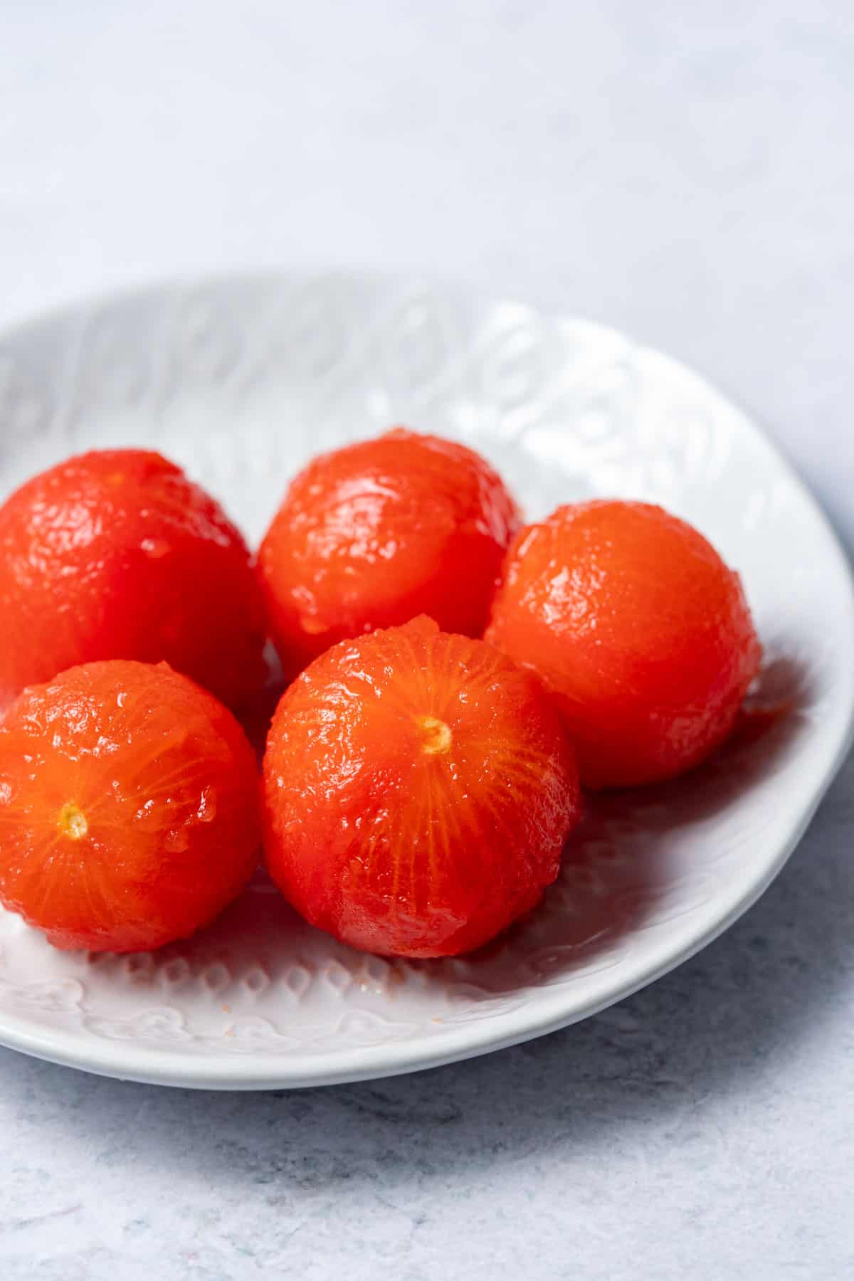 image of 5 peeled tomatoes on a white plate