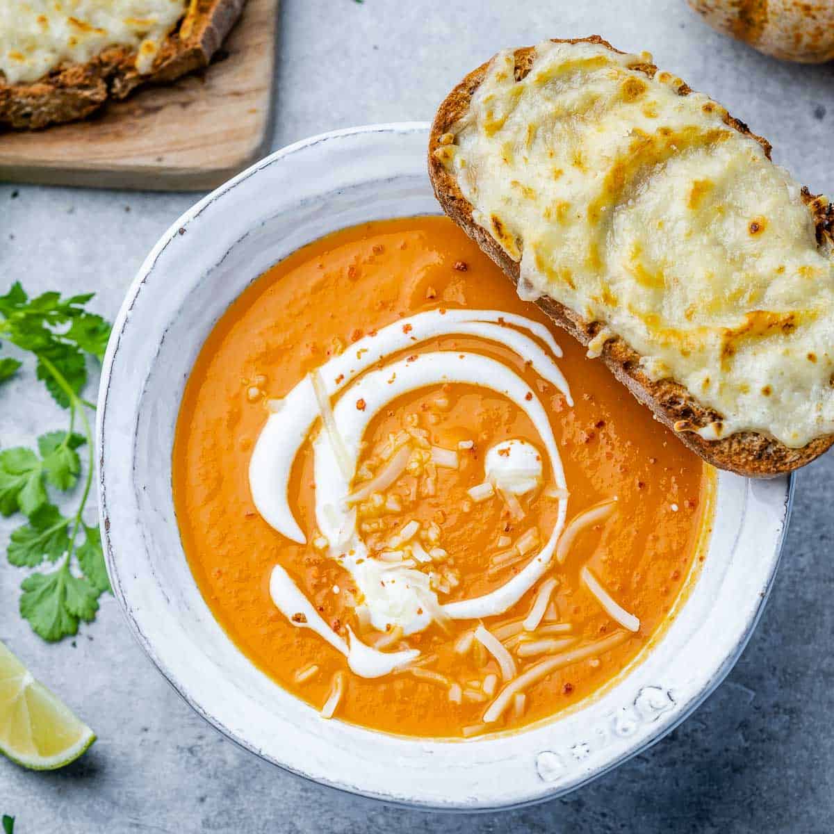 top view butternut squash soup in a white bowl with grilled cheesy bread over bowl