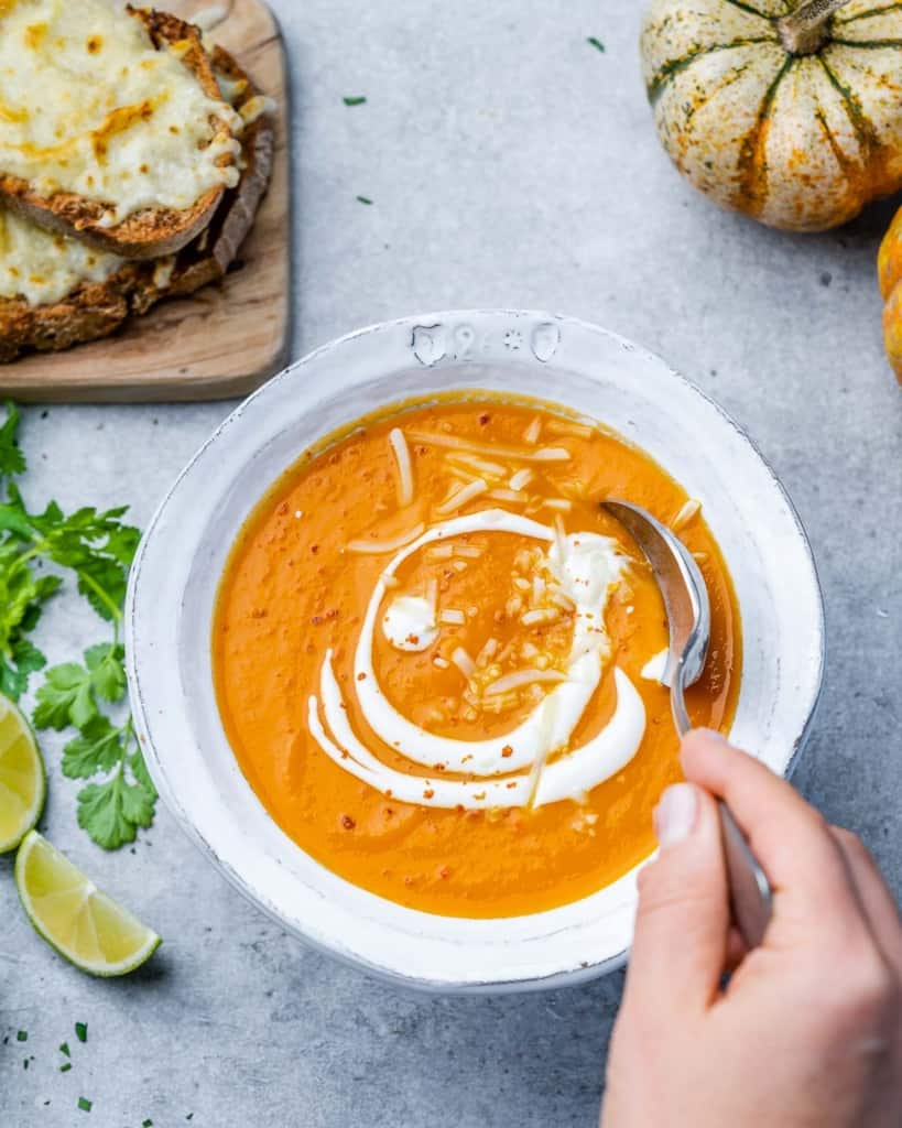 hand holding spoon in butternut squash soup bowl