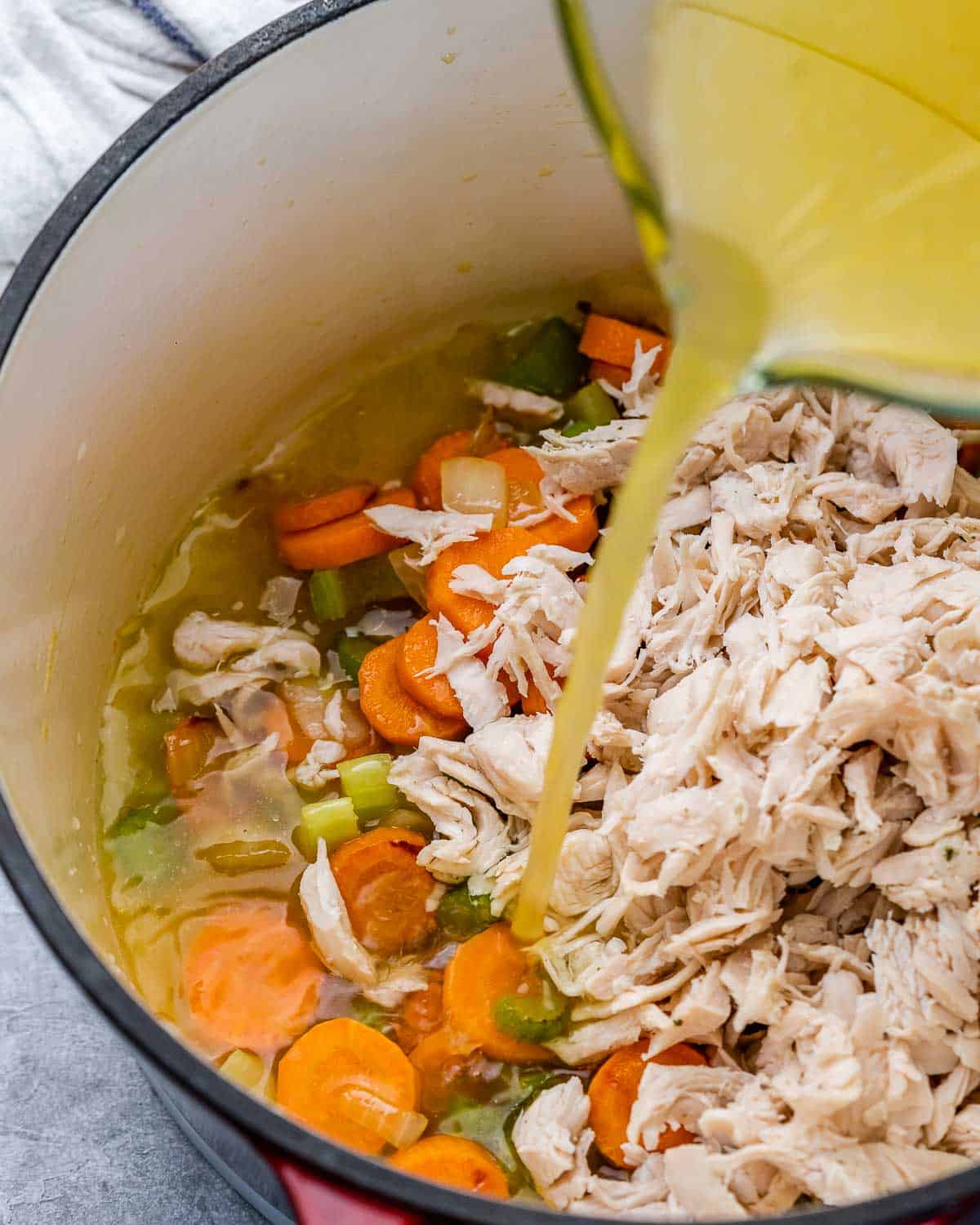 Pouring broth into a pot with turkey and vegetables.