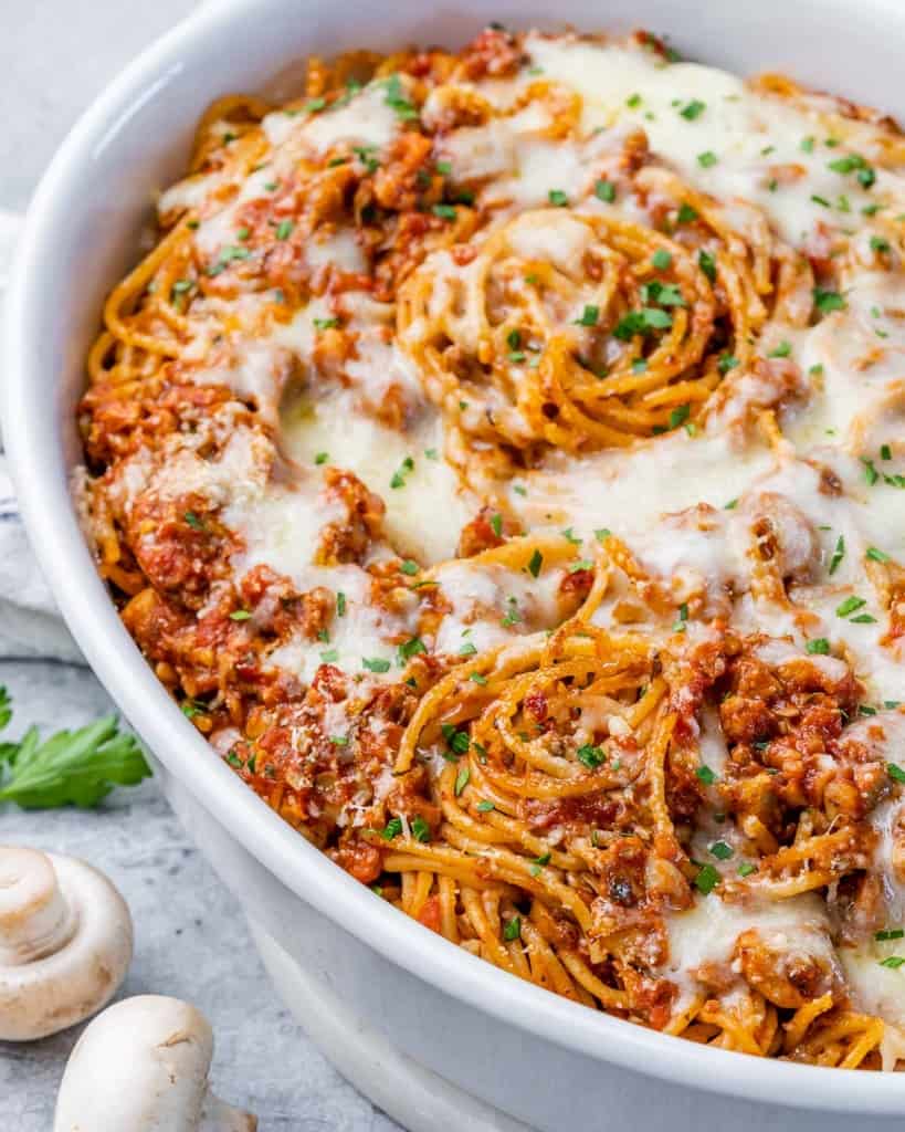 White casserole dish with spaghetti noodles, sauce and cheese.