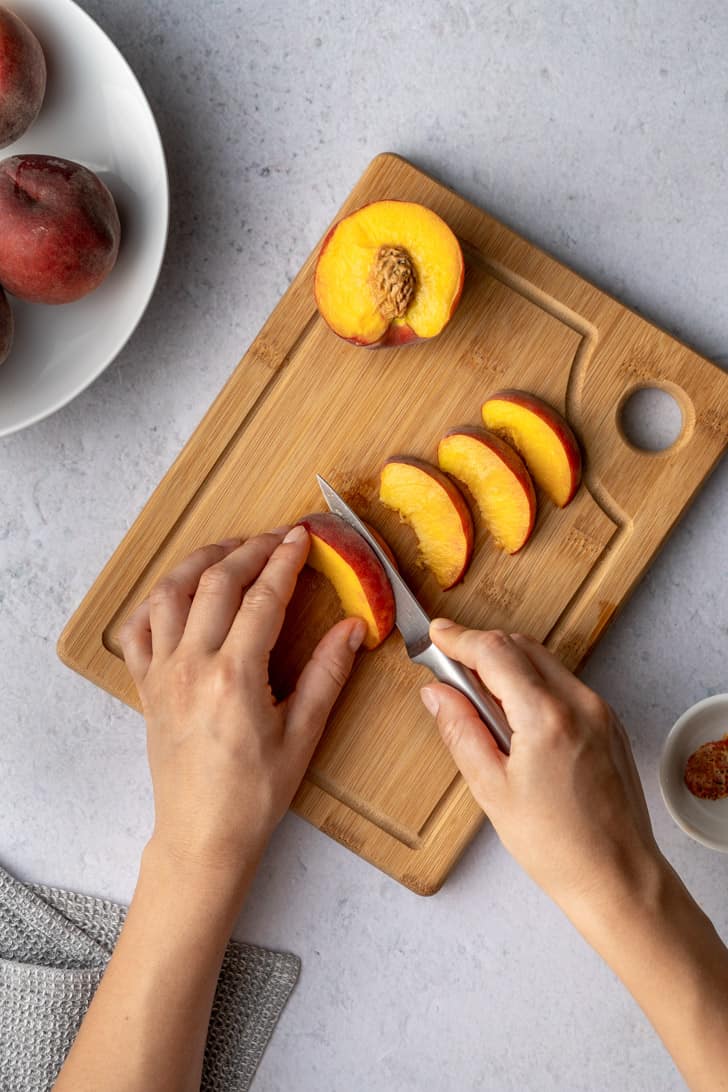 slicing the peach atop a cutting board 