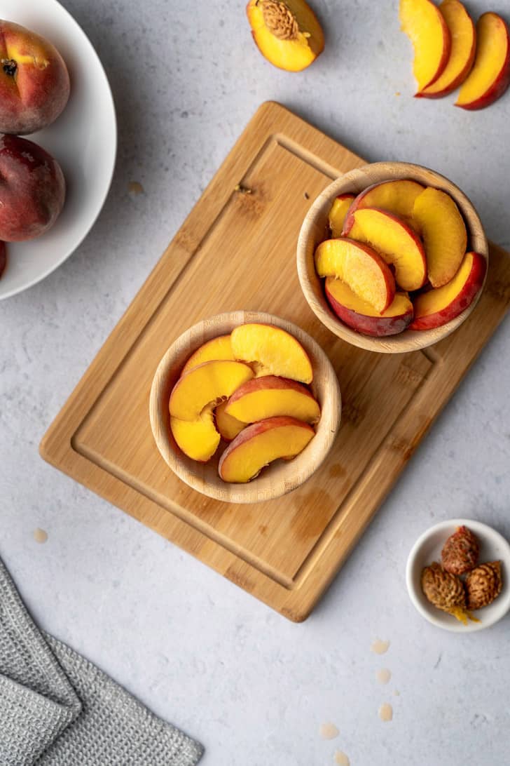 sliced peaches in two bowls atop cutting board