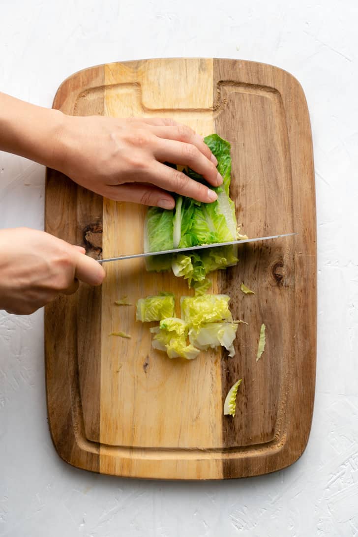 slicing romaine lettuce on cutting board with knife 