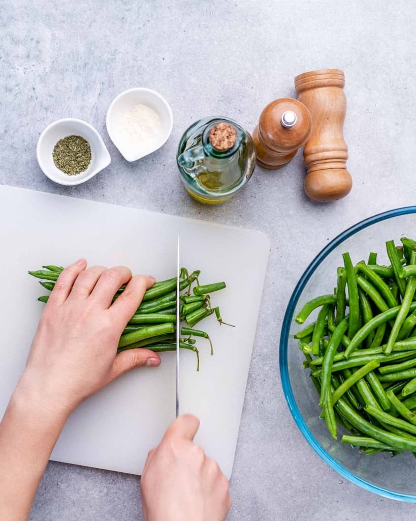 hand cutting the trims off green beans on a white cutting board
